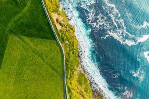 Satellite view of a road dividing seaside on right and green pasture on left.