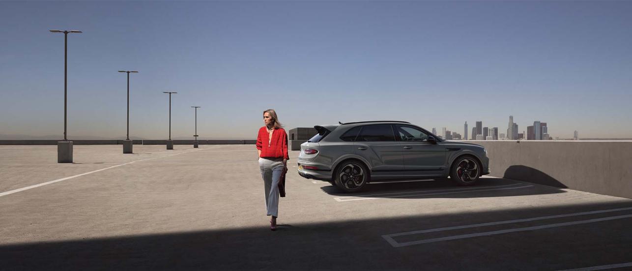 Front side angled view of Bentley Bentayga Speed in Orange Flame colour featuring Matt black matrix grille and 22 inch Alloy wheels driving along a highway.