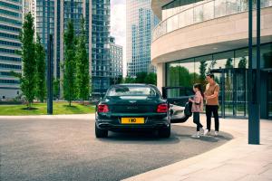 Rear view of Bentley Flying Spur in Verdant Green, with right passenger door open, parked with buildings and two people in view